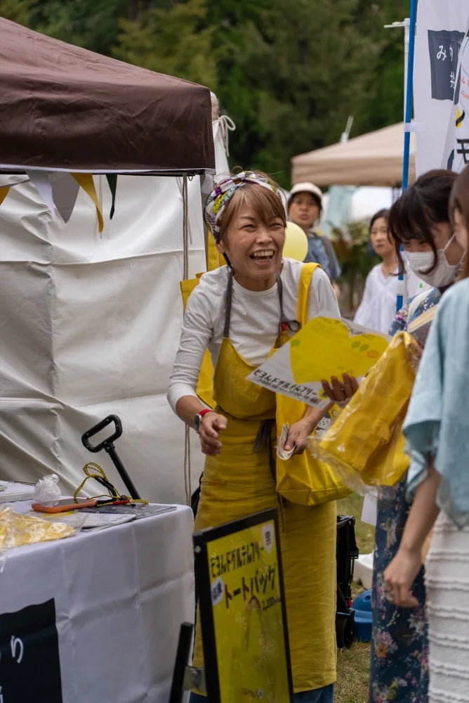 第1回の会場で、笑いながらトートバッグを手渡す発起人naco
